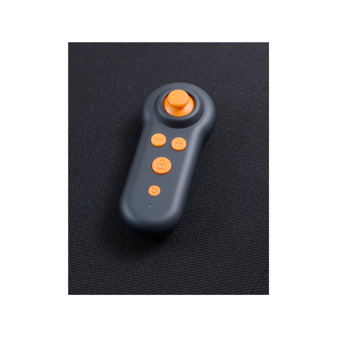 A sleek black and orange wireless remote, with four circular buttons and a joystick, lies on a dark textured surface. Its an ideal accessory from Golden Tech for the Ally Powerchair, enhancing functionality with style.